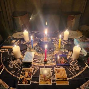 Puede incluir: Una escena m&iacute;stica con velas encendidas, cartas del tarot y un altar central. La disposici&oacute;n incluye velas de varios colores, barajas de tarot y un mantel oscuro con s&iacute;mbolos celestiales. El ambiente es tenue, creando una atm&oacute;sfera espiritual.