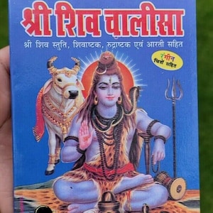 May include: A blue book titled Shri Shiv Chalisa featuring an illustration of the deity Shiva sitting in a meditative pose with a cobra around the neck, a white bull, a trident, and a small drum on a patterned ground with Hindi text.
