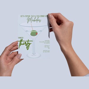 Può includere: Un biglietto d'invito bianco con un'illustrazione di bicchiere da martini, oliva e testo. Il testo recita "IT'S TIME TO CELEBRATE Michelas", "DIRTY Thirty" e i dettagli dell'evento. Il biglietto è tenuto da due mani su sfondo grigio chiaro.