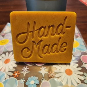 May include: A yellow bar of soap with the words "Hand Made" embossed on it.