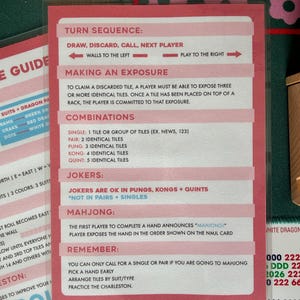 May include: A pink and white Mahjong game rules card with text detailing turn sequence, combinations, and jokers. The card provides instructions for gameplay, including how to make an exposure and announce "Mahjong!"