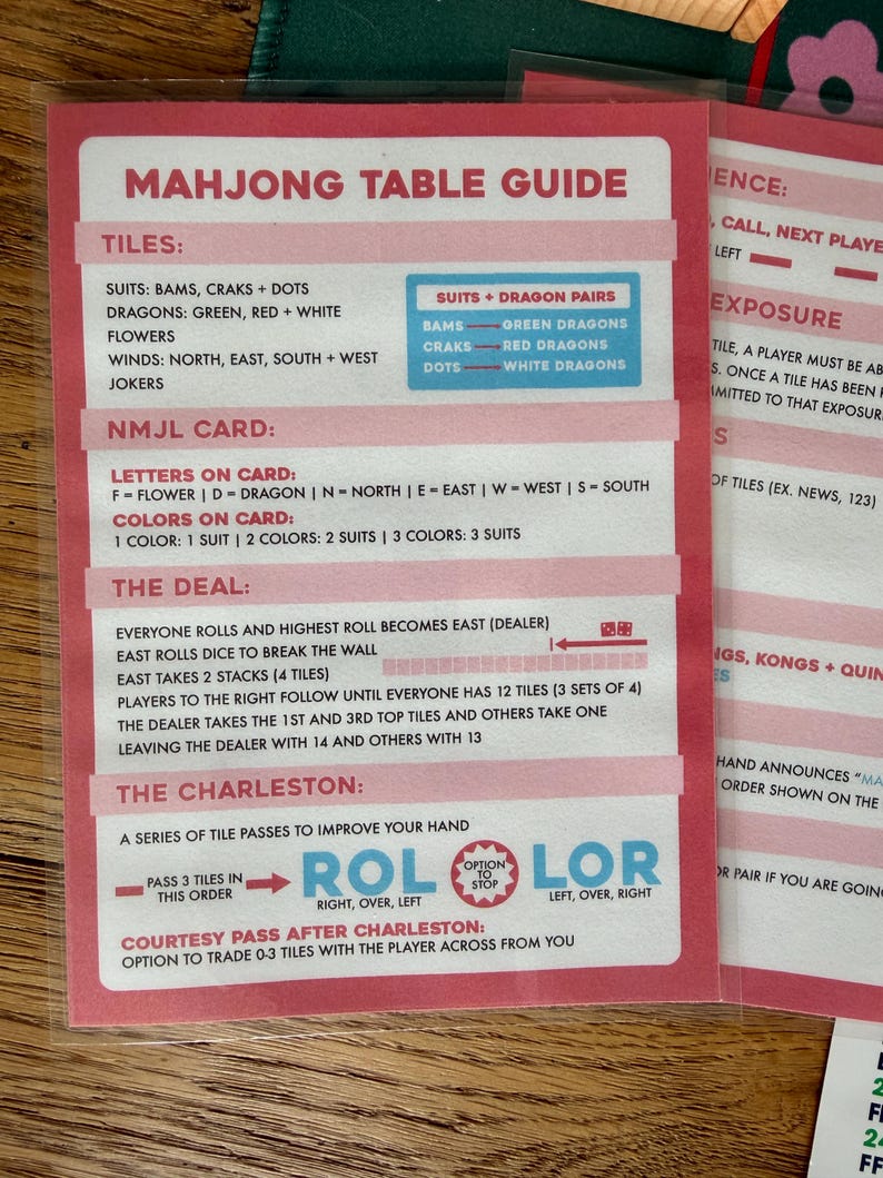 May include: A pink and white Mahjong Table Guide card with detailed instructions. The guide lists tiles, suits, and card information. The card also includes instructions for The Deal and The Charleston.