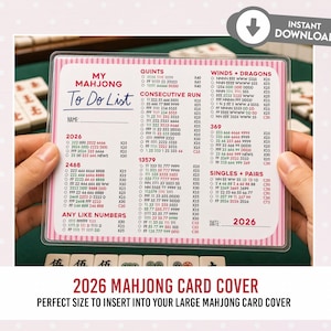 May include: A pink and white Mahjong To Do List card with a clear plastic cover. The card includes sections for Quint, Consecutive Run, and Singles & Pairs. The text "2026" is visible. The card is held by two hands.