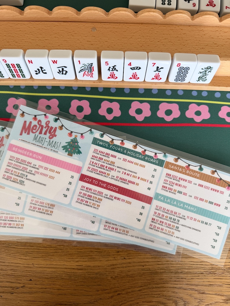 Pu&ograve; includere: Una scheda segnapunti plastificata per Mah Jongg intitolata Merry Mahj-Mas con grafiche a tema natalizio, tra cui luci a stringa e un albero di Natale. La scheda elenca varie combinazioni di mani come Reindeer Run e Santa's Route con i punti.