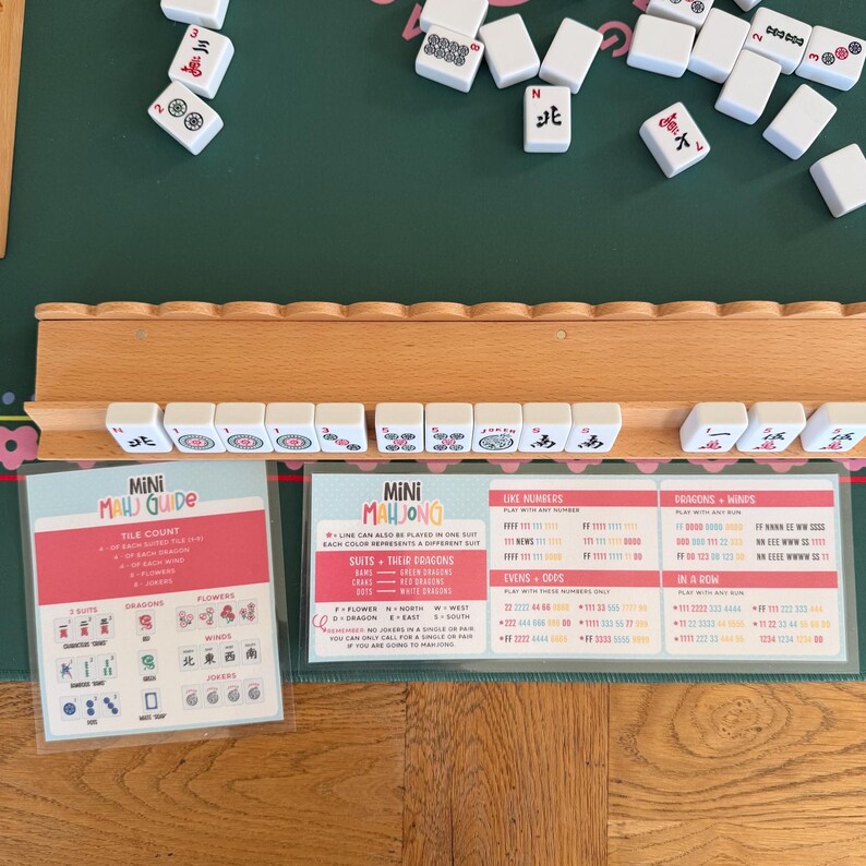 Peut inclure: Un support de tuiles de mah-jong en bois contenant des tuiles blanches avec divers symboles, accompagn&eacute; de deux cartes d'instructions intitul&eacute;es Mini Mahjong Guide. Les cartes pr&eacute;sentent des tableaux de comptage, de suites et de r&egrave;gles.