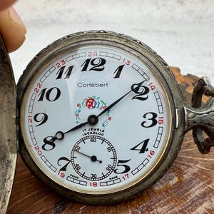May include: A white ceramic mug with a black handle and the text "But First, Coffee" in a bold, black font. The mug is set against a blurred background, suggesting a cozy setting.