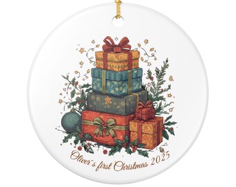 May include: White ceramic Christmas ornament featuring a stack of illustrated gift boxes in shades of orange, blue, and red, adorned with bows and festive greenery. The text "Oliver's first Christmas 2025" is printed on the ornament.