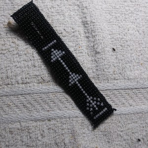 May include: A black beaded bracelet with a white arrow design.