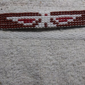 May include: A beaded bracelet with a brown, white, and red pattern. The bracelet has a blue and green border.
