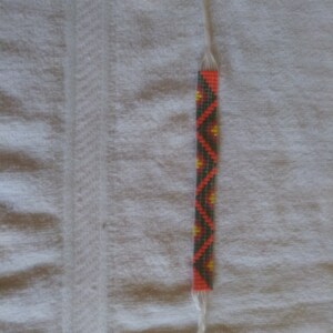 May include: A beaded bracelet with a geometric pattern in black, orange, red, and yellow.