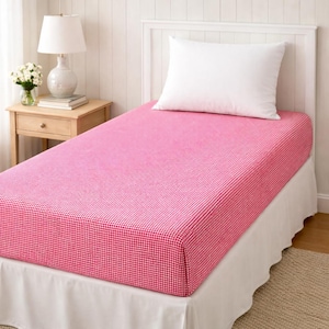 May include: A twin-sized bed with a fitted sheet in a red and white gingham pattern. A white pillow rests on the bed. The bed is against a white headboard and a white bed skirt.