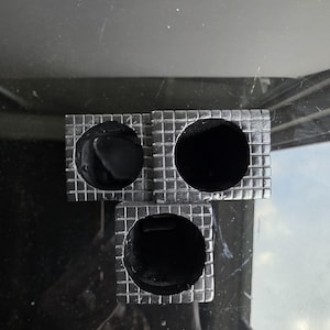 May include: Three square, silver-colored objects with a grid pattern, each containing a large, round, black hole. The objects are arranged in a triangular shape. The background is a dark, reflective surface.