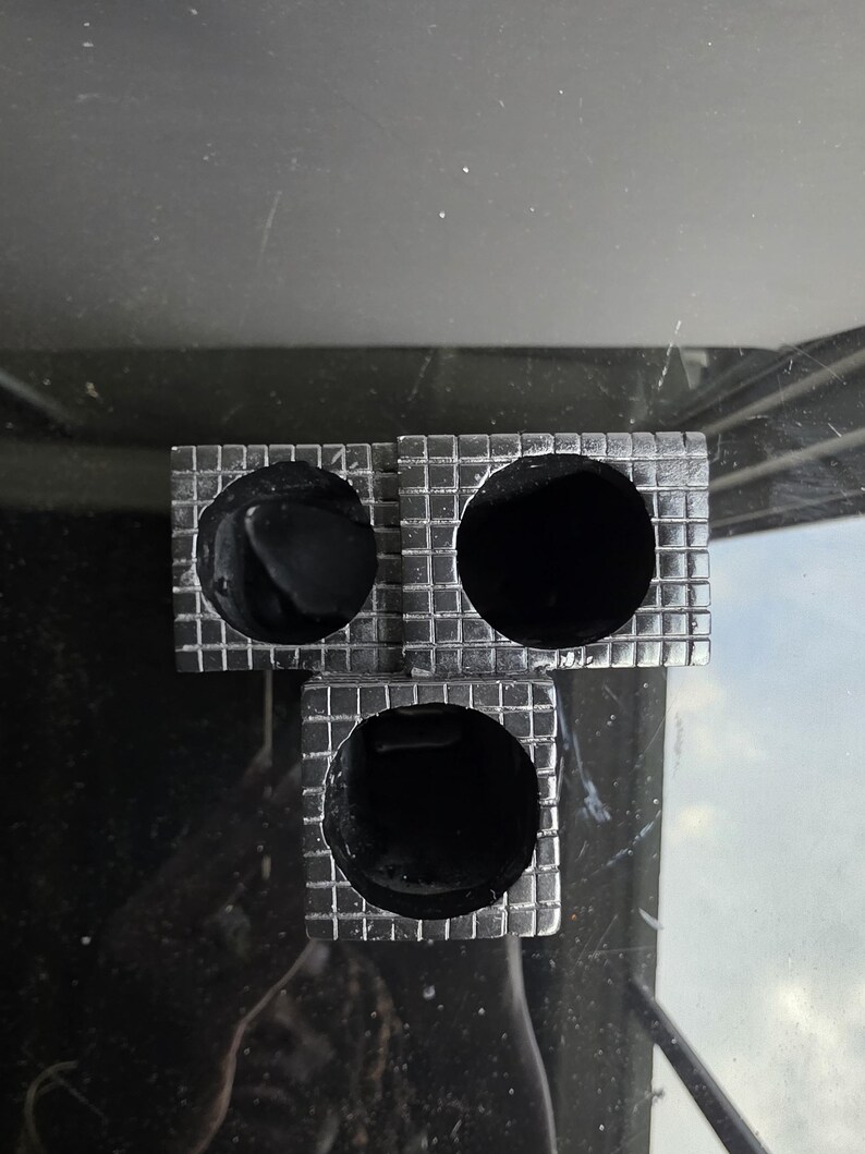 May include: Three square, silver-colored objects with a grid pattern, each containing a large, round, black hole. The objects are arranged in a triangular shape. The background is a dark, reflective surface.