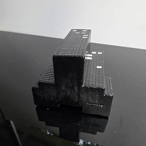 May include: A black, tiered soap dish with a textured, brick-like pattern. The soap dish has a rectangular shape with a few white accents. The text "Hand Wash Only" is visible on the side.