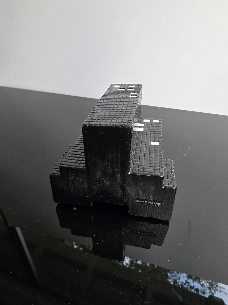May include: A black, tiered soap dish with a textured, brick-like pattern. The soap dish has a rectangular shape with a few white accents. The text "Hand Wash Only" is visible on the side.