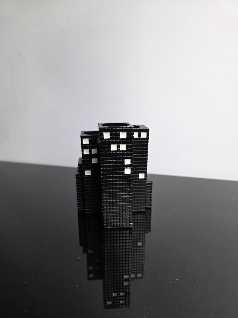 May include: A black, miniature cityscape sculpture with white square windows. The buildings are arranged in a cluster, reflecting on a glossy black surface. The sculpture has a textured surface.
