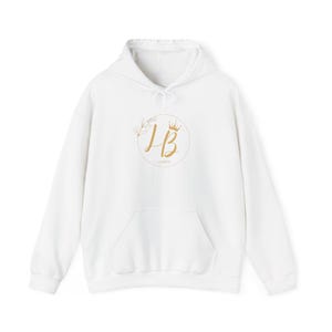 May include: White hooded sweatshirt with a front pocket and a drawstring. The front features a gold circular design with the letters "LB" and a crown, surrounded by floral elements. The word "AMBER" is below the letters.