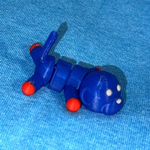 May include: A blue articulated toy insect with red accents on its legs and antennae. The toy has a rounded head with white dots and is posed on a blue fabric surface. The toy is a fun, creative item.
