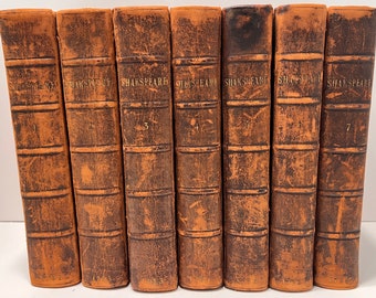 Op de afbeelding: Een set van zeven antieke, in leer gebonden boeken met de titel "Shakespeare" gegraveerd op de ruggen. De boeken zijn genummerd van 1 tot en met 7.