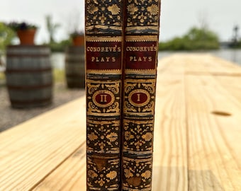 May include: Two antique books with gold and black patterned covers. The books are titled "Congreve's Plays" and are labelled with Roman numerals I and II.