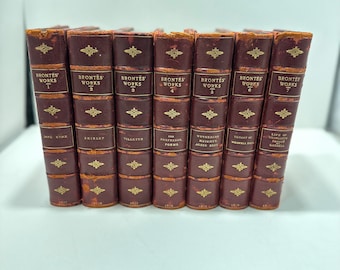 May include: A set of seven antique books bound in brown leather. The spines are embossed with "BRONTË'S WORKS" and volume numbers. Titles include "JANE EYRE" and "SHIRLEY". The spines feature gold decorative details.