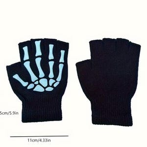 K&ouml;nnte beinhalten: Ein Paar schwarze fingerlose Handschuhe mit einem wei&szlig;en Skeletthand-Motiv auf dem Handr&uuml;cken eines Handschuhs. Die Handschuhe sind 15 cm hoch und 11 cm breit, wie durch die sichtbaren Messlinien und den Text angegeben.