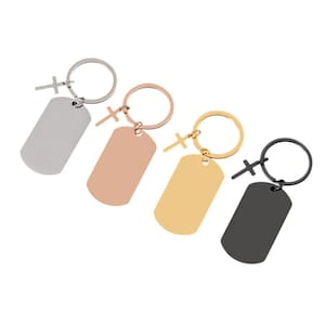 May include: Four metal keyrings in silver, rose gold, gold, and black. Each keyring has a dog tag shape and a small cross charm. The key rings are round.