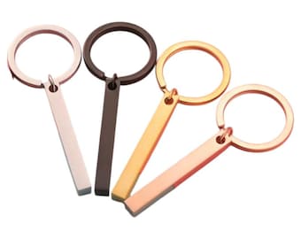 May include: Four metal keyrings with a bar-shaped charm. The keyrings are in rose gold, gold, silver, and black.