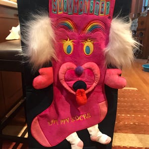 May include: A pink sock monster Christmas stocking with white fur ears, rainbow embroidery, and the text "Sock Monster Eat My Socks".