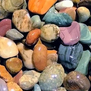 May include: A collection of smooth, polished river rocks in various colors, including orange, green, brown, and purple. The stones have a glossy finish and vary in size and shape, creating a natural, textured appearance. Ideal for decorative purposes or crafts.