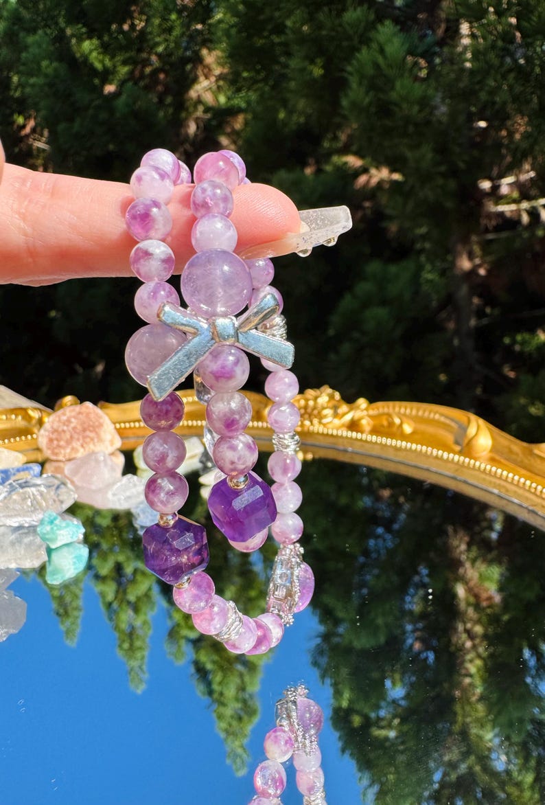 May include: Two purple and pink gemstone bracelets with a silver bow charm. The bracelets are made of round and square beads.