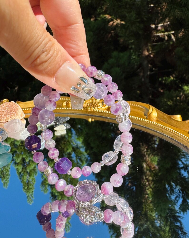 May include: Two purple and clear crystal bracelets with silver accents. The bracelets are made of amethyst and clear quartz beads.