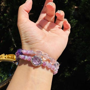 May include: A set of three bracelets featuring amethyst and clear quartz beads. The middle bracelet has a large amethyst gemstone with a silver setting.