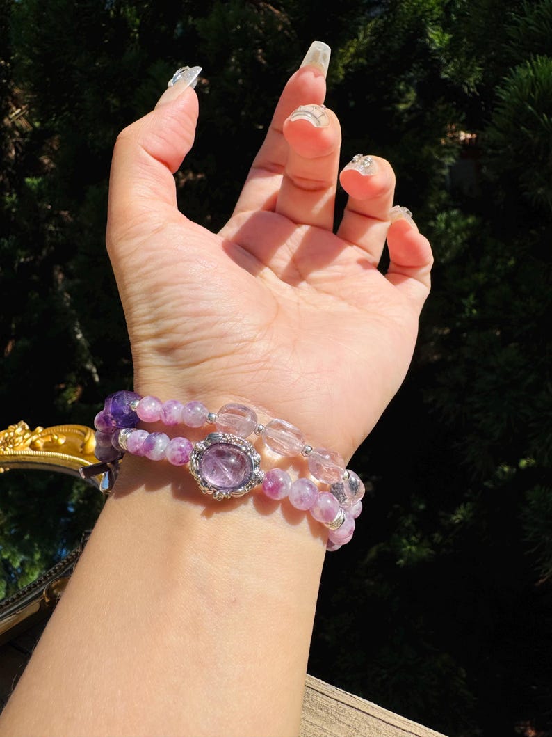 May include: A set of three bracelets featuring amethyst and clear quartz beads. The middle bracelet has a large amethyst gemstone with a silver setting.