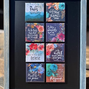 Op de afbeelding: Een ingelijst kunstwerk met acht vierkante tegels, elk met een inspirerende quote en bloemmotieven. De tegels zijn in een raster gerangschikt, elk met een andere boodschap in elegant schrift. Het frame is lichtblauw.