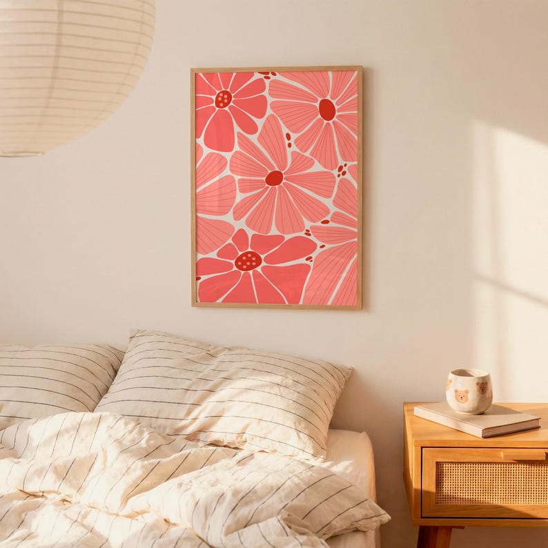 May include: A framed floral art print featuring a repeating pattern of large, stylized pink flowers with red centers against a white background. The artwork is in a wooden frame and hangs on a cream-colored wall.