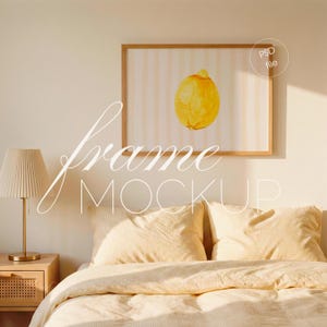 Op de afbeelding: Een ingelijste aquarelprint van een citroen hangt boven een bed met gele beddengoed en kussens. Het kunstwerk toont een gele citroen tegen een gestreepte achtergrond. Links staan een lamp en een nachtkastje. De woorden "frame MOCKUP" zijn over elkaar heen geplaatst.