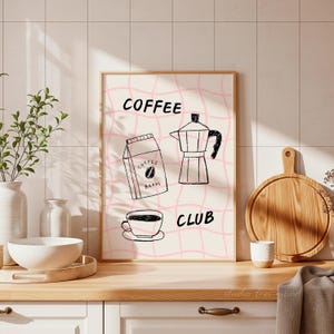 May include: A framed print with a pink grid background and the words "COFFEE CLUB". The print features illustrations of a coffee bag, a coffee maker, and a coffee cup. The artwork is in black and white.