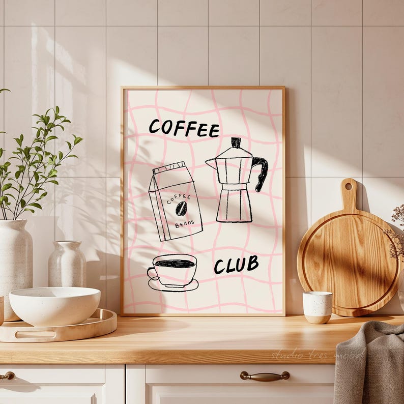 May include: A framed print with a pink grid background and the words "COFFEE CLUB". The print features illustrations of a coffee bag, a coffee maker, and a coffee cup. The artwork is in black and white.