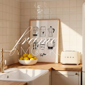 May include: A kitchen interior with a framed print displaying coffee-themed illustrations. A white bowl of lemons sits near a white sink and a cream-coloured toaster. The print has the word "Coffee" at the bottom.