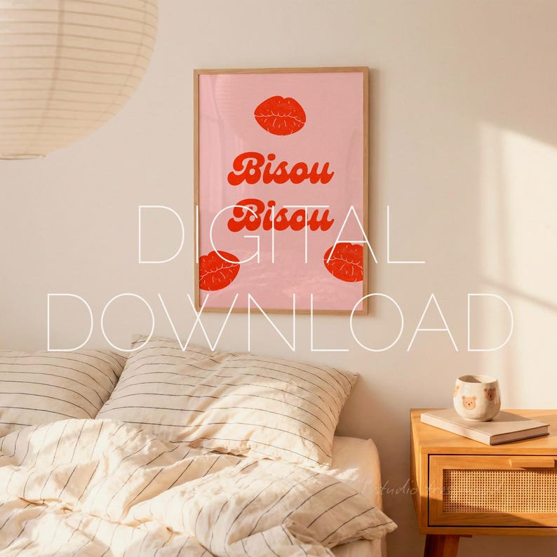 May include: A framed pink art print with the words "Bisou Bisou" in red script, along with three red lip illustrations. The artwork is displayed above a bed with striped bedding and a wooden nightstand.