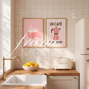 May include: Two vertical rectangular wall art prints in light wooden frames. The left print features a pink checkered coffee cup. The right print displays a pink moka pot with the text UN CAFÉ POR FAVOR. The frames are mounted on a white tiled wall.