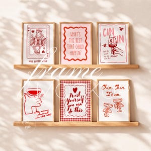 Pode incluir: Seis quadros decorativos dispostos em duas prateleiras de madeira. As impressões apresentam ilustrações em vermelho e rosa, incluindo uma carta de rainha, taças de vinho e textos como 'What's the best that could happen?', 'Trust yourself' e 'Chin Chin Team'.