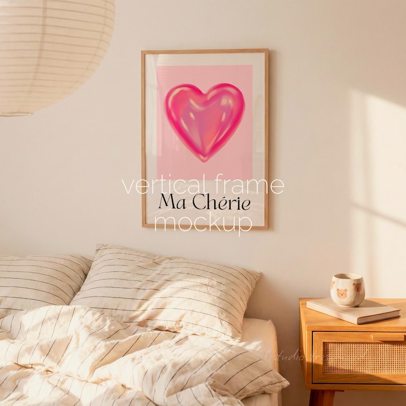 May include: A framed vertical art print featuring a glossy pink heart on a light pink background. The words "vertical frame Ma Ch&eacute;rie mockup" are printed in white below the artwork. The frame is a light wood color.
