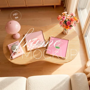 Puede incluir: Una mesa rosa claro con dos maquetas enmarcadas, una lámpara rosa, un libro y un jarrón con flores. Los marcos tienen fondos rosas con gráficos. El libro se titula "Flower Market". La lámpara es de color rosa claro.