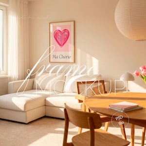 May include: A framed print featuring a pink heart graphic with the text "Ma Chérie" on a light pink background. The artwork hangs above a white sectional sofa in a bright, airy room. A wooden table and chairs are in the foreground.