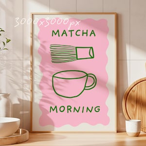 May include: A framed art print with a pink background and green illustrations. The print features a matcha whisk and a teacup, with the words "MATCHA" and "MORNING" in green. The artwork is displayed in a light-colored wooden frame.