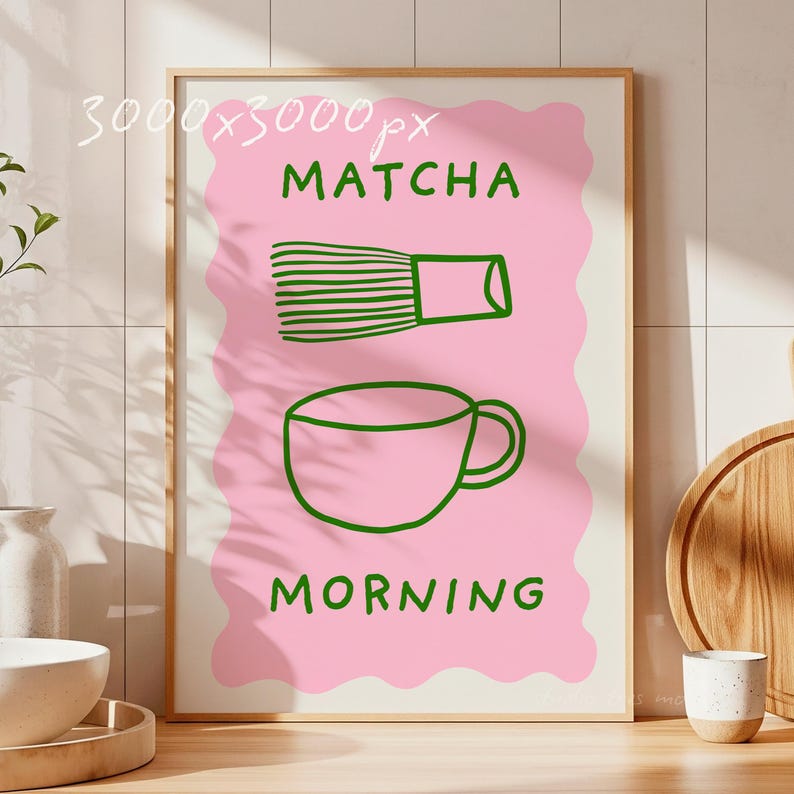 May include: A framed art print with a pink background and green illustrations. The print features a matcha whisk and a teacup, with the words "MATCHA" and "MORNING" in green. The artwork is displayed in a light-colored wooden frame.