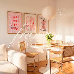 Può includere: Una scena interna luminosa con opere d'arte incorniciate con testo rosa e rosso, un tavolo bianco e sedie in vimini. L'arte include frasi come "good mood" e "cin cin". Un vaso di fiori bianchi aggiunge un tocco fresco.