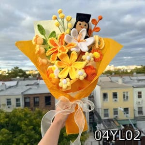 Crochet graduation bouquet in orange and yellow shades with lily-shaped crochet flowers, accented with golden ribbon.